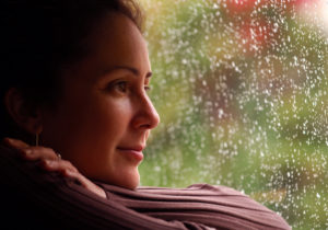 hopeful woman looking outside window while its raining