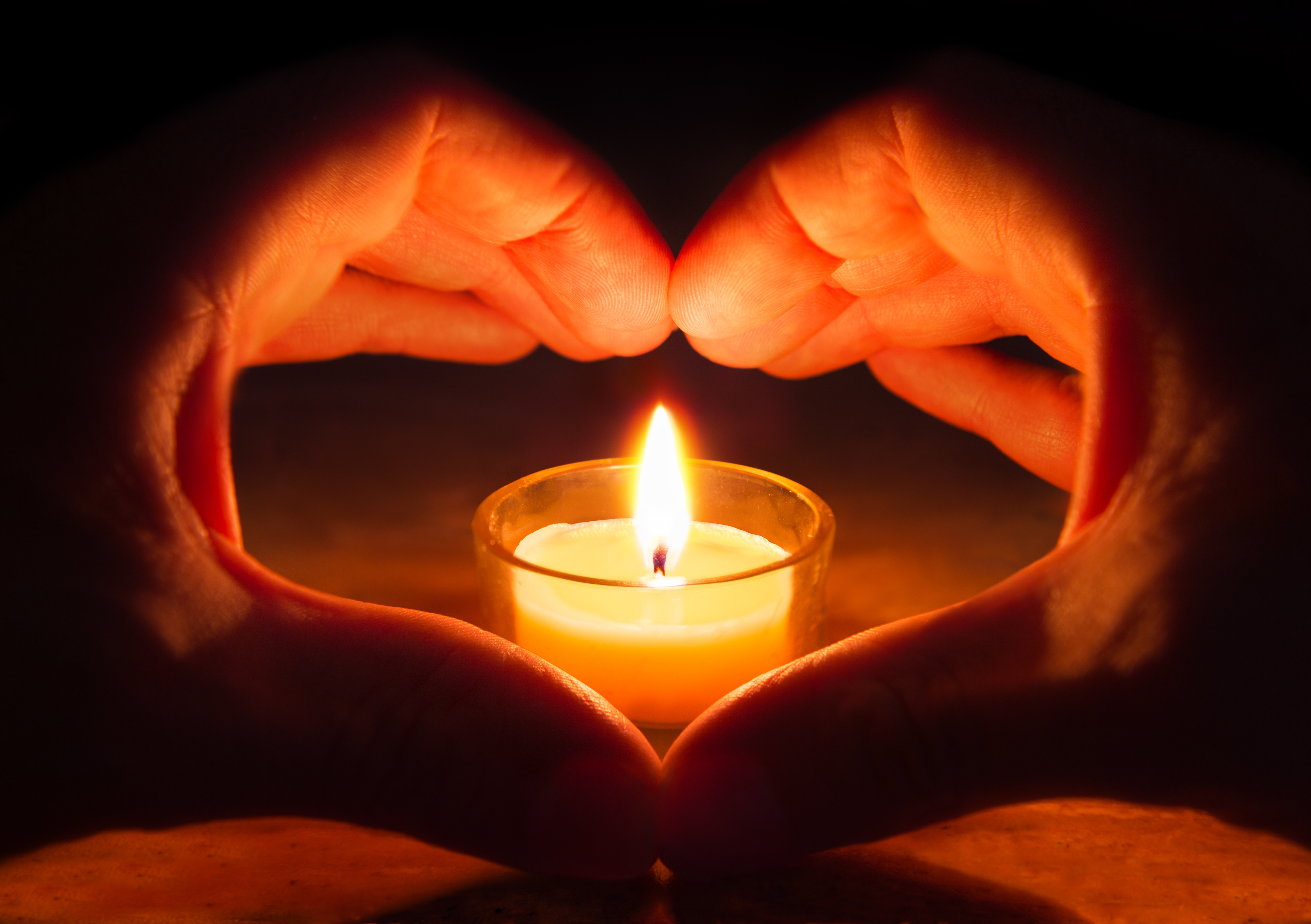 Hands forming heart around a candle