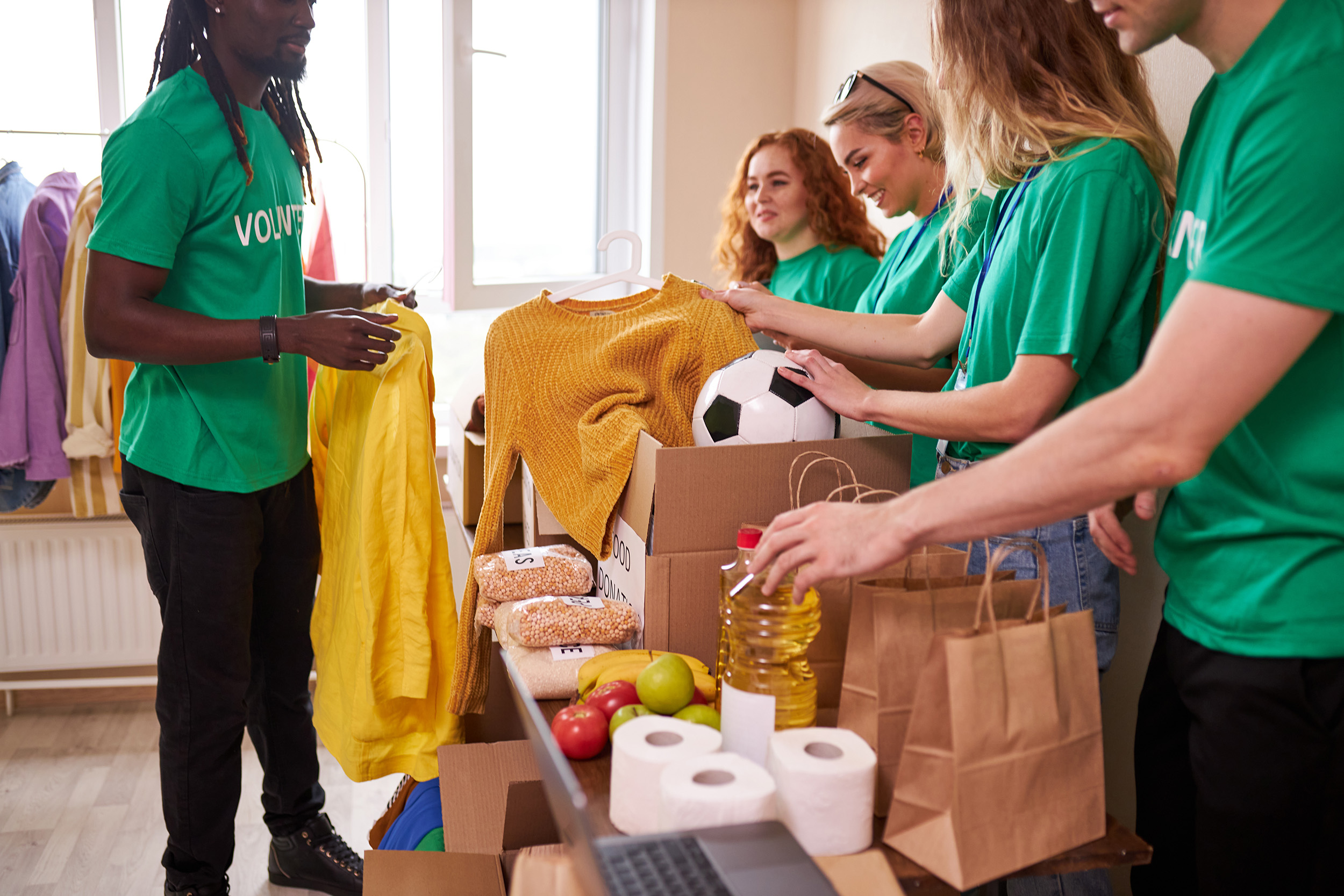 group of diverse people working in charitable foundation, happy caucasian and african volunteers looking at donation box, separating donations stuffs