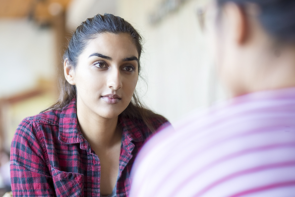 Concentrated Indian woman talking to friend. Serious young student looking at companion. They discussing strategy. Communication concept